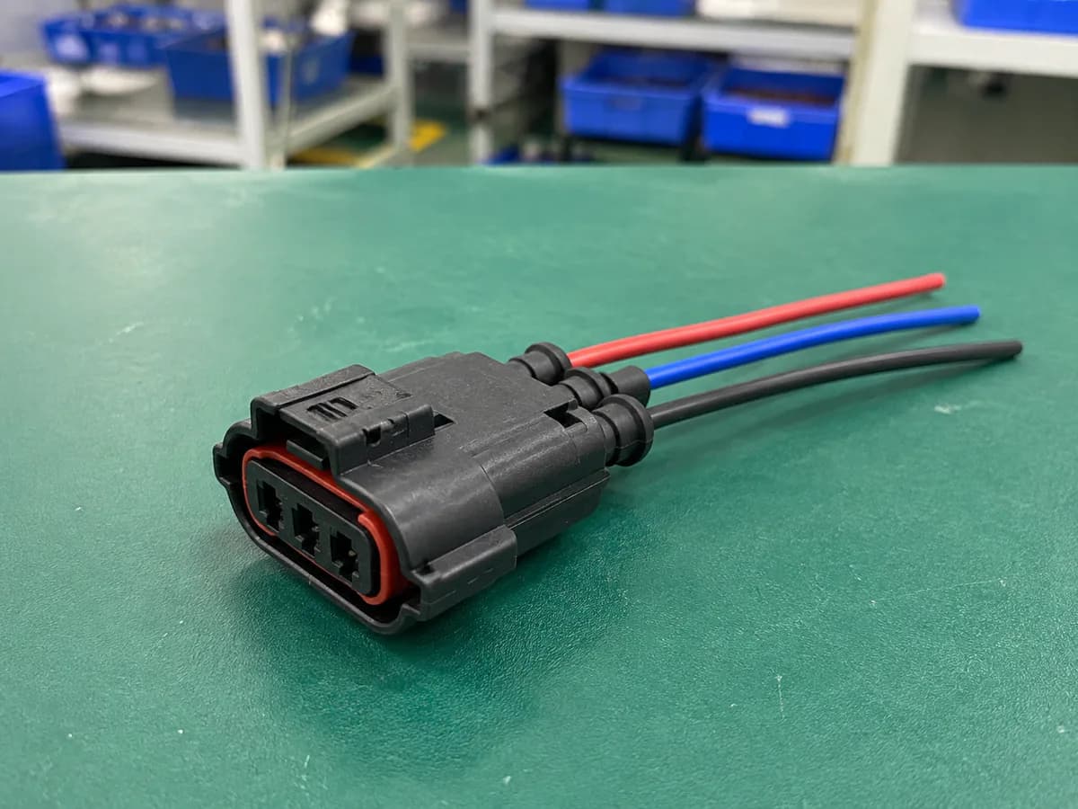 simple sealed three-position automotive connector lead on a green factory workbench